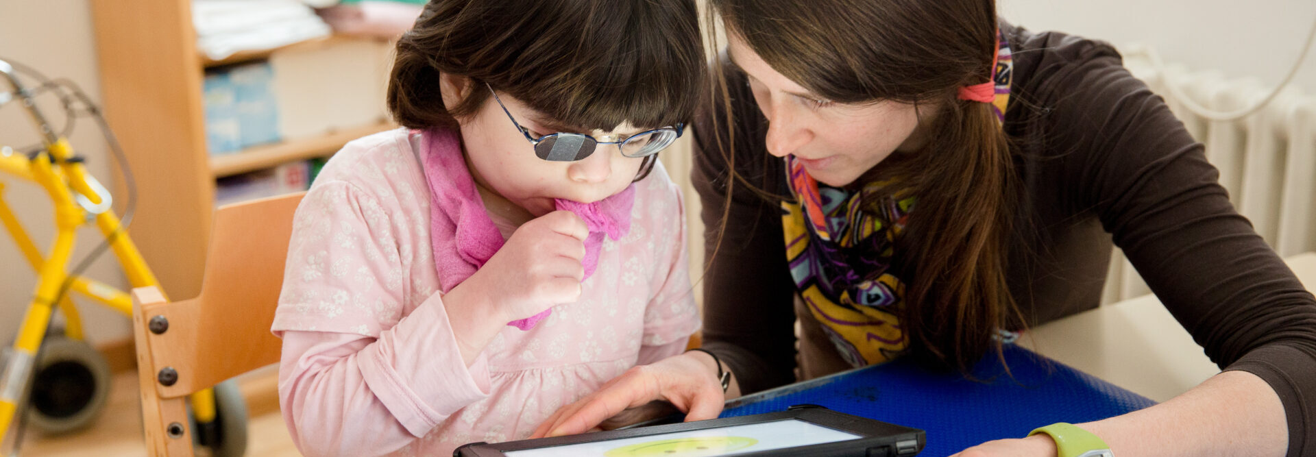 Bambina che lavora su un tablet supportata dall'insegnante. La tavoletta mostra una grande faccina gialla.